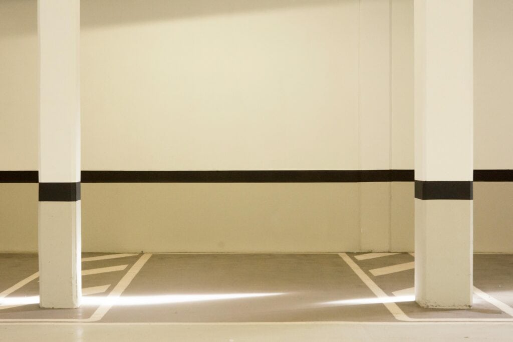 A minimalist view of a well-lit, empty parking garage interior featuring structural posts.